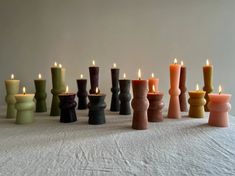 many different colored candles are lined up in a row on a white tablecloth,