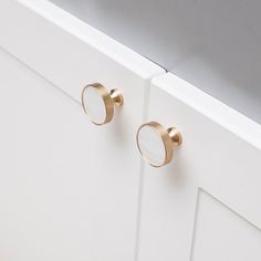 two brass knobs on the side of a white cabinet