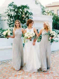 three bridesmaids in grey dresses holding hands and smiling at each other while standing outside