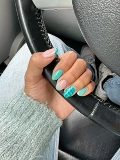 a woman's hand with blue and green nail polish holding a black steering wheel