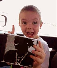 a young boy holding up a book in the back seat of a car with his hand out