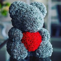 a gray teddy bear with a red heart on it's chest sitting on a table