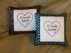 two pillows with embroidered hearts and the words friends forever on them are sitting on a bed