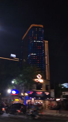 a city street at night with cars and buildings lit up in bright blue, red, and white lights