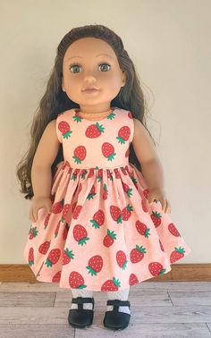 an american girl doll wearing a pink dress with red strawberries on it, standing in front of a white wall