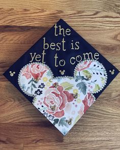 the best is yet to come graduation cap on top of a wooden table with flowers