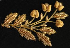 a gold brooch with leaves is shown on a black velvet surface, close up