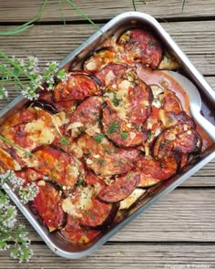 a pan filled with cooked vegetables on top of a wooden table next to some flowers