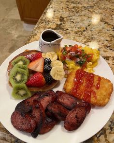 a white plate topped with meat, fruit and pastry next to a cup of coffee