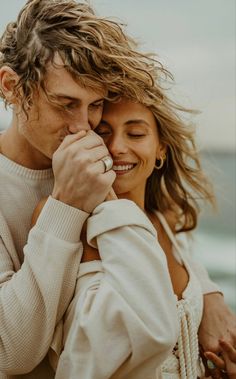 a man and woman standing next to each other near the ocean smiling at each other