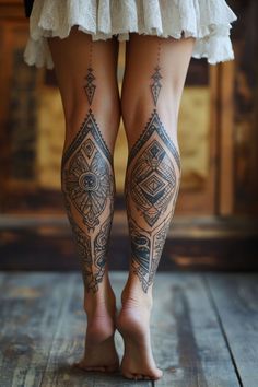 the legs and ankles of a woman with tattoos on her body, standing in front of a wooden floor