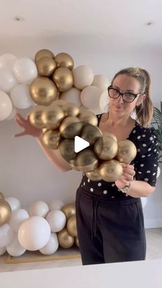 a woman is holding balloons in front of a wall with gold and white balls on it