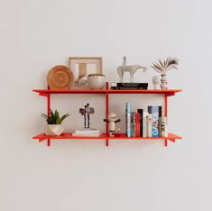 two orange shelves with books, plants and pictures on them are against a white wall