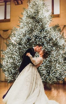 a bride and groom kissing in front of a christmas tree