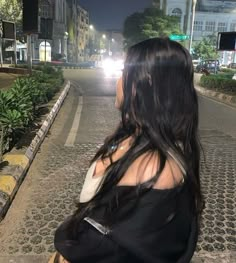 a woman standing on the side of a road at night with her back to the camera