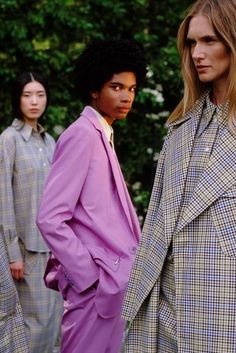 three models standing in front of trees wearing purple coats and plaid pants, all looking off to the side