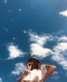 a woman in a hat talking on her cell phone under a blue sky with white clouds