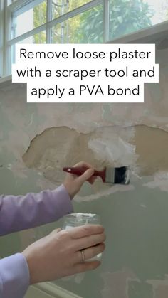 a woman using a paint brush to remove loose plaster from a wall that has been stripped off