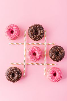 four donuts with pink glaze and chocolate sprinkles arranged on sticks