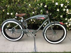 a gray and white bike with a shark on the front tire is parked in front of some bushes