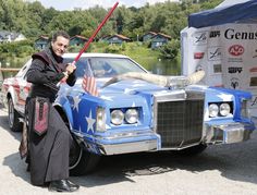 a man dressed in an american flag outfit holding a bat next to a blue car