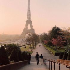 two people walking down a path in front of the eiffel tower