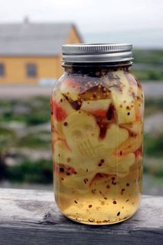 a jar filled with lots of food sitting on top of a wooden table next to a yellow house