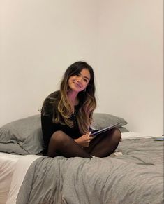 a woman sitting on top of a bed with her legs crossed and holding a book