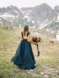 a woman in a blue dress holding a bouquet of flowers on top of a mountain