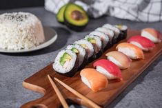 sushi on a wooden board with chopsticks next to rice and avocado