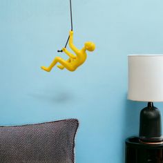 a yellow figure hanging from a string on a blue wall next to a black lamp