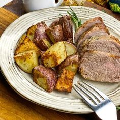 a white plate topped with meat and potatoes next to a cup of coffee on a wooden table