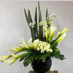 a black vase filled with yellow and white flowers