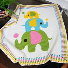 an elephant crocheted blanket on top of a wooden table next to a potted plant