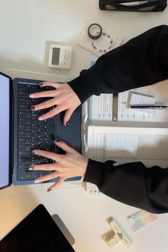 two hands on the keyboard of a laptop computer next to papers and other office supplies