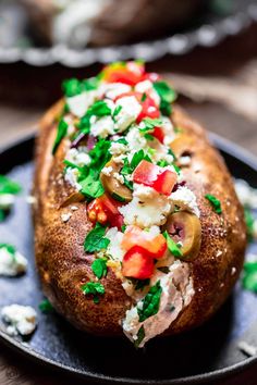 a baked potato with vegetables and feta cheese on it sitting on a black plate