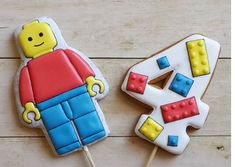 a lego man cookie next to a decorated number 4 cookie on a wooden table with white and blue icing