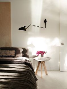 a bedroom with a bed, table and lamp on the wall next to each other