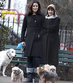 two women standing next to each other on a bench with three dogs in front of them