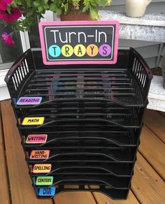 a stack of black plastic trays sitting on top of a wooden floor next to a potted plant