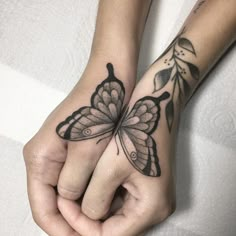 two people holding hands with tattoos on their fingers and one has a butterfly tattoo on it