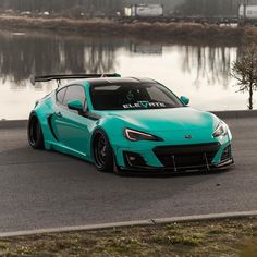 a blue sports car parked in front of a body of water