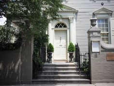 a white door is on the side of a gray house with steps leading up to it