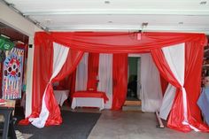 a red and white canopy bed with drapes on the top is set up for a party