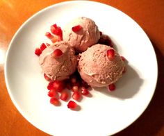 three scoops of ice cream and pomegranate on a white plate with wood table