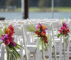 rows of white chairs with colorful flowers on the back one row is filled with pink, orange and purple orchids