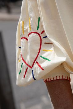 a woman's white dress with red, yellow and green hearts on it