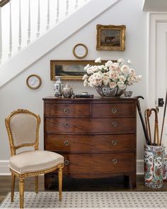 an old dresser with flowers and vases on it in front of a stair case