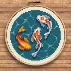 a cross stitch pattern with two gold and white koi fish in the water on a wooden background