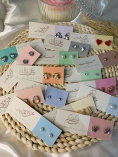 a basket filled with lots of different types of earrings on top of a table next to a cupcake